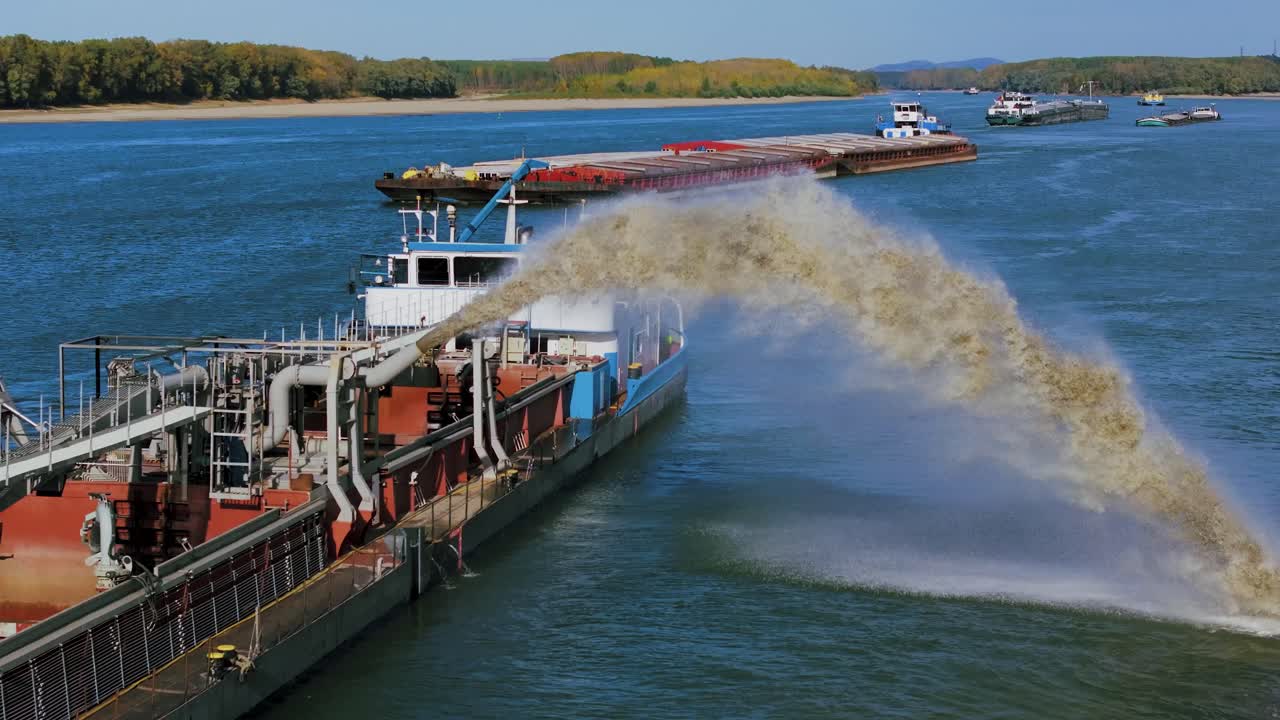 Aerial close up shot of a dredger unloading dredged sand on a big river, other ships passing by, sunny day