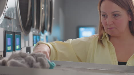 professional operator in yellow shirt uses towel to carefully remove lint dirt from washer filter, ensuring cleanliness, industrial laundry machine during service routine in modern laundromat