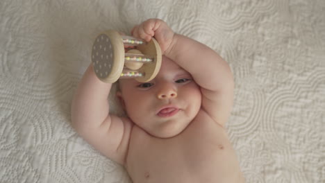 newborn baby playing with toy in white bed sheets, bright bedroom