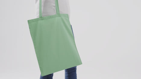 caucasian woman wearing white hoodie holding green bag on white background, copy space, slow motion