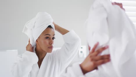 african american woman in bathrobe touching her head looking in the mirror at bathroom