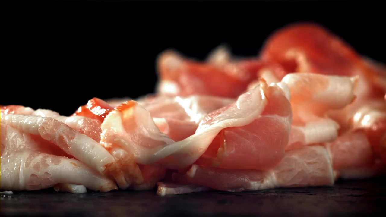 Fette di pancetta cruda che cadono al rallentatore su sfondo nero