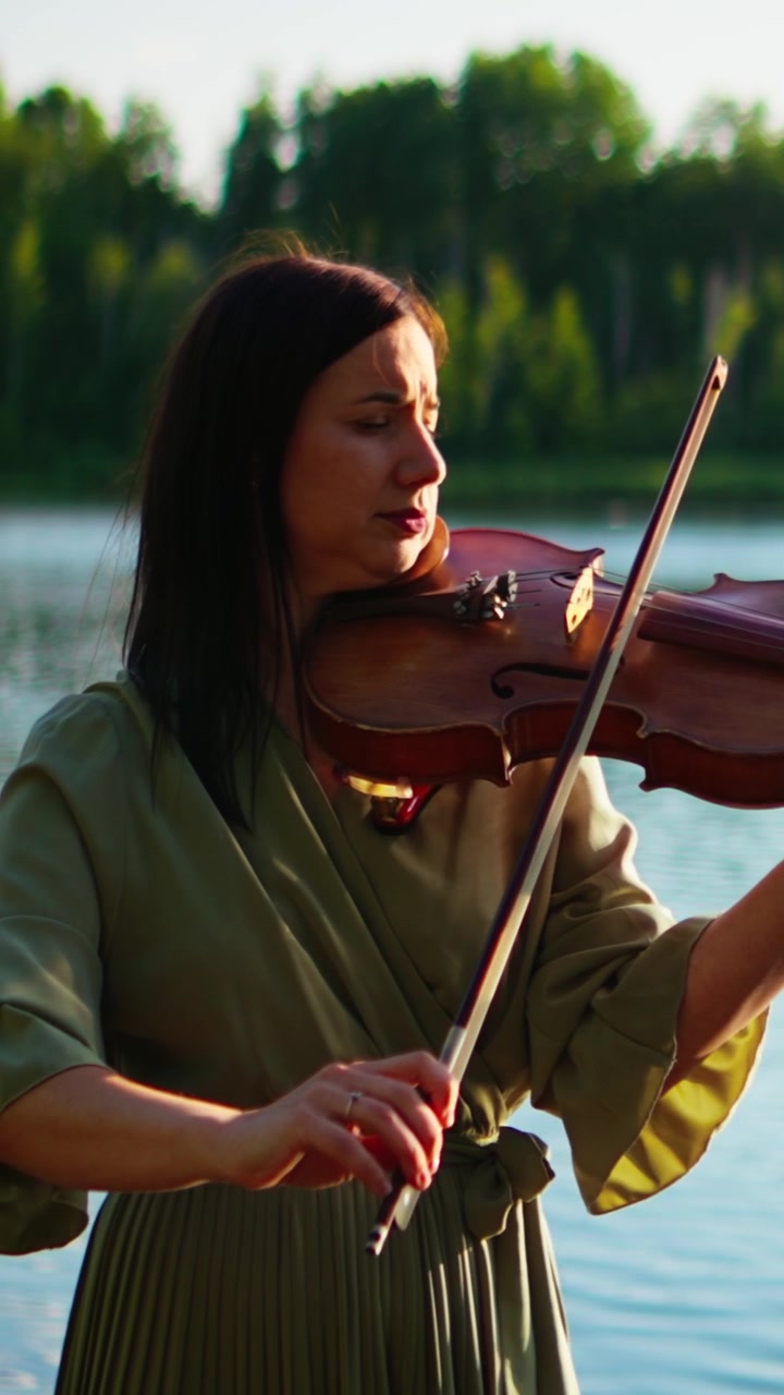 Woman Playing Violin Outdoors by a Lake at Sunset