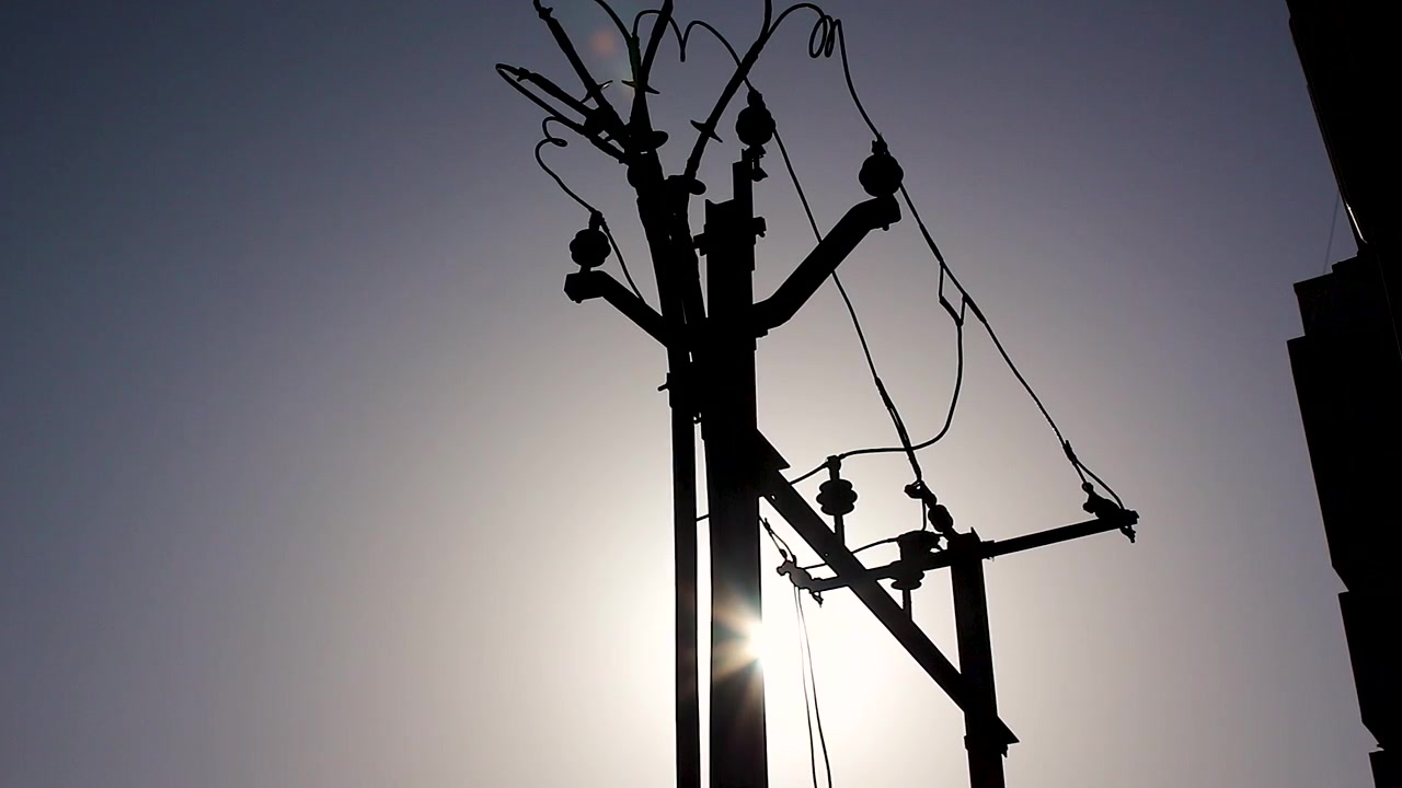 Dramatic silhouette of utility pole and overhead power lines against bright sky. Ideal for electricity, energy infrastructure, power supply, grid and utility industry projects.