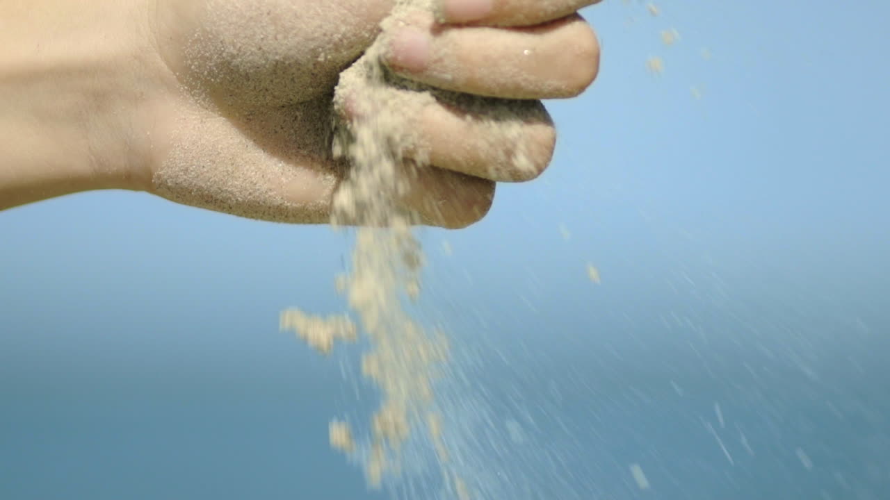 Sand Falls From Woman’s Hand Against Blue Sky in Slow Motion, Close Up
