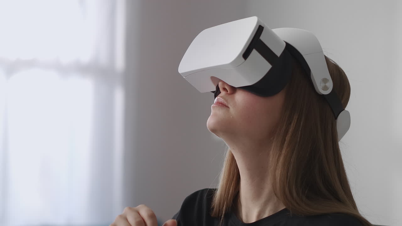 la usuaria está usando una nueva pantalla montada en la cabeza para jugar juegos sentada en la sala de estar y moviendo las manos para controlar la tecnología moderna