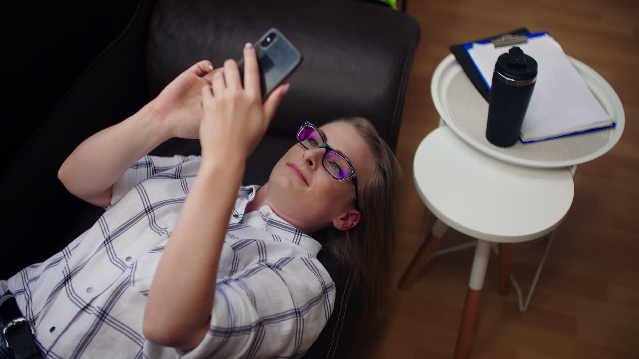 Attractive Businesswoman Having Video Call On Mobile Phone While Lying On Sofa At Office 2
