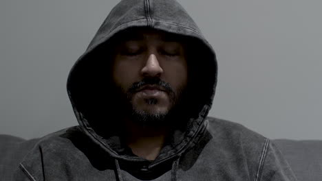 a close up shot of the face of an indian man wearing a hoodie, dollying out as he remains motionless with his eyes closed as he calmly meditates in complete silence