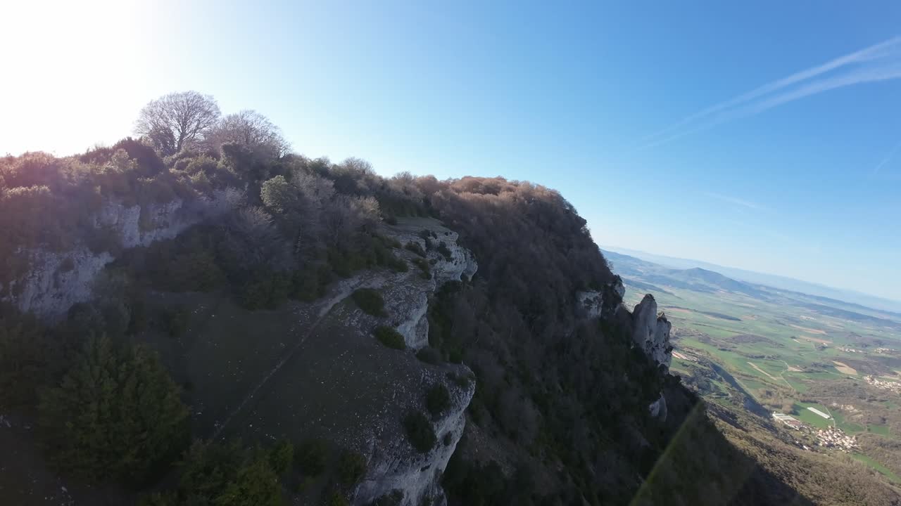Drone image flying along the edge of a rocky cliff. Relaxing slow-motion footage, sunny day, forested area, mountain summit. Precipice