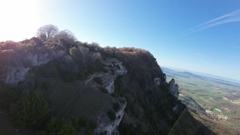 drone image flying along the edge of a rocky cliff. relaxing slow-motion footage, sunny day, forested area, mountain summit. precipice