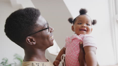 father playing game with baby daughter and lifting her in air in loft apartment