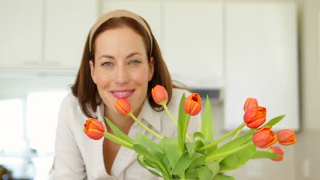 Pretty-woman-smelling-her-vase-of-tulips-and-smiling-at-camera