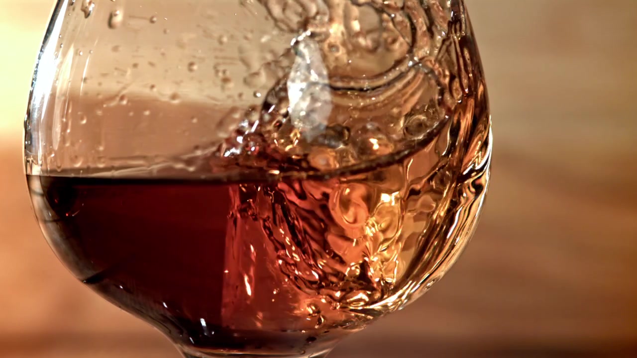 Cubetto di ghiaccio che cade in un bicchiere di vino rosso al rallentatore