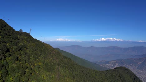 teleféricos que suben y bajan por el tranvía en la ladera de una colina con las montañas del himalaya al fondo