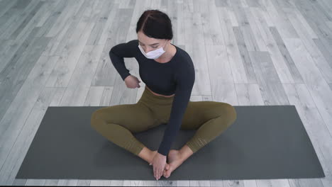 jonge vrouw doet yoga oefeningen, mediteert in lotushouding, draagt medisch gezichtsmasker. vrouwelijke atleet binnenshuis.