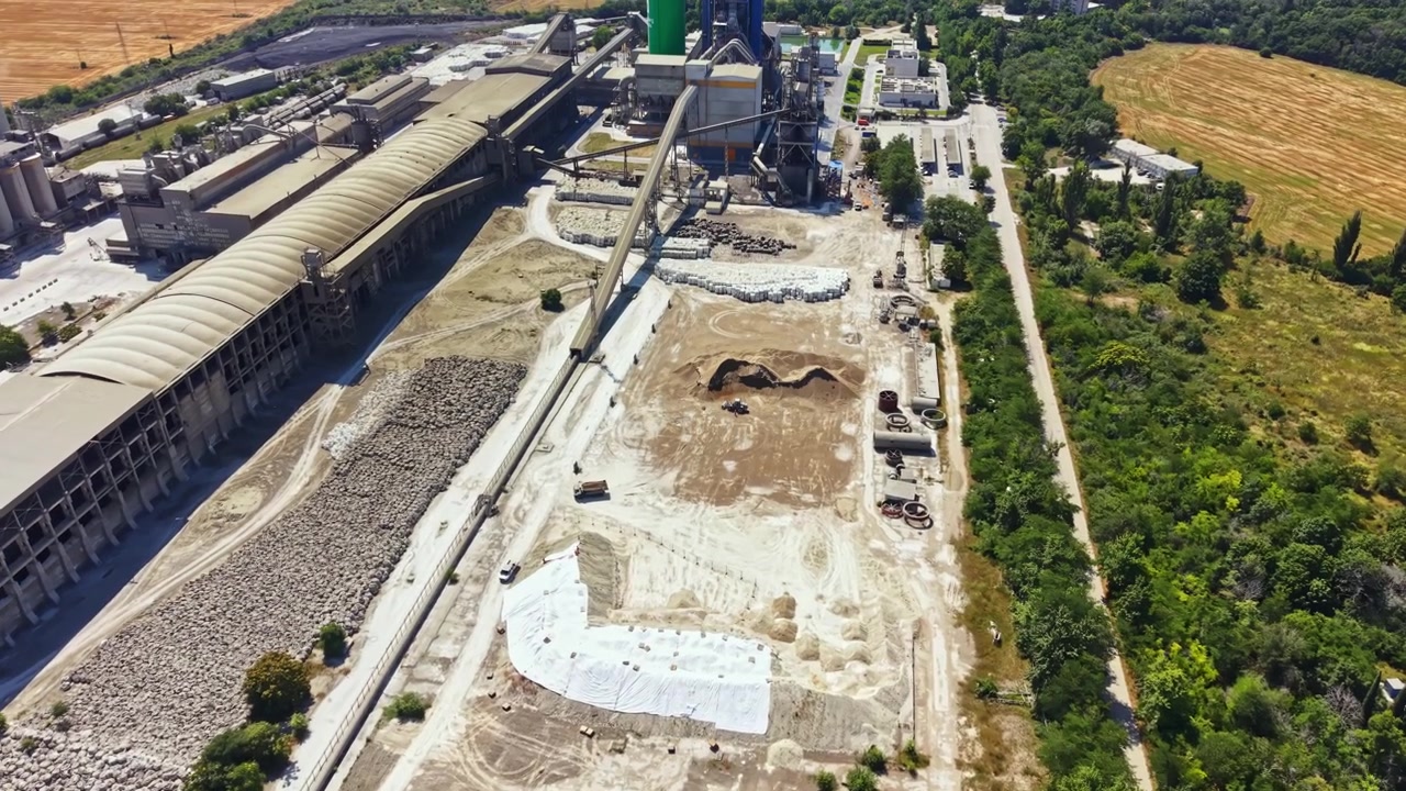 Industrial site with buildings, storage areas, and open land in a rural setting during daytime