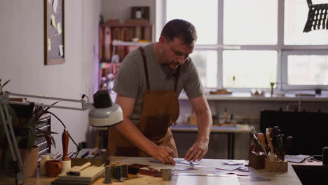 leathersmith cuts leather sheet with cutter at workplace