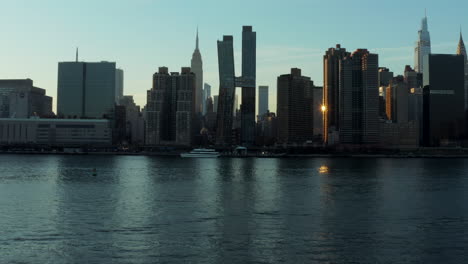 Fly-over-cruise-boat-floating-on-river.-Silhouettes-on-high-rise-apartment-buildings-on-waterfront.-Manhattan,-New-York-City,-USA