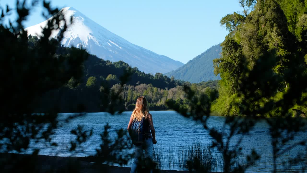 una mujer excursionista está de pie en la costa del lago con el volcán de osorno en el fondo, chile