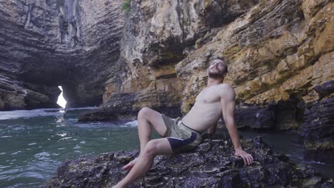 handsome attractive male sitting on a rock in the sea.