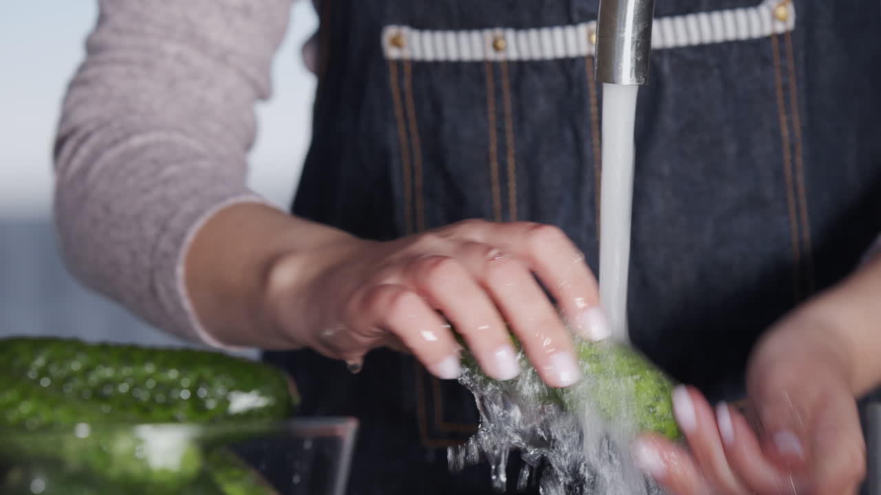 una mujer lava pepinos bajo un chorro de agua de un grifo 1