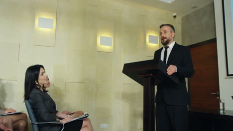 camera going round the audience and male business speaker on the podium who is talking in a conference room