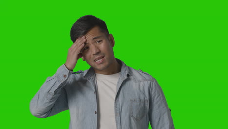 Studio-Shot-Of-Casually-Dressed-Stressed-Young-Man-With-Headache-Against-Green-Screen-