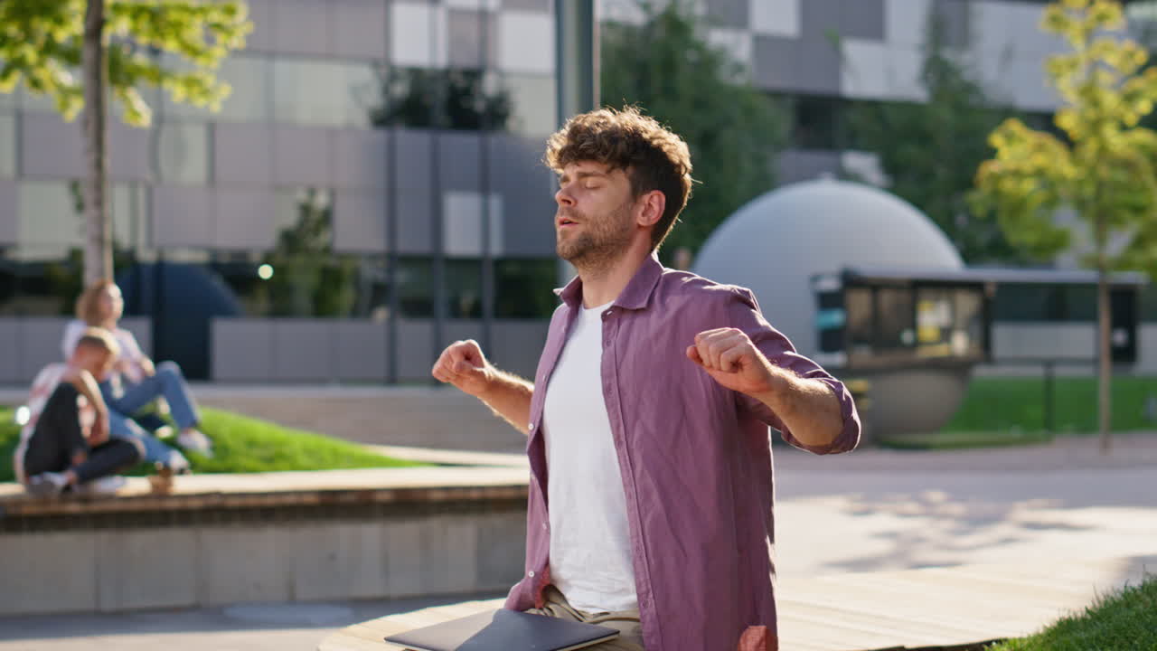 un tipo casual cerrando su computadora portátil sintiendo alivio. un trabajador independiente con barba rizada estirándose.
