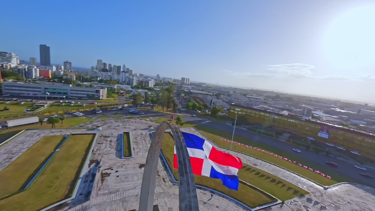 Fpv flight over city of Santo Domingo during beautiful sunny day at Plaza de la Bandera - Traffic on roundabout in capital
