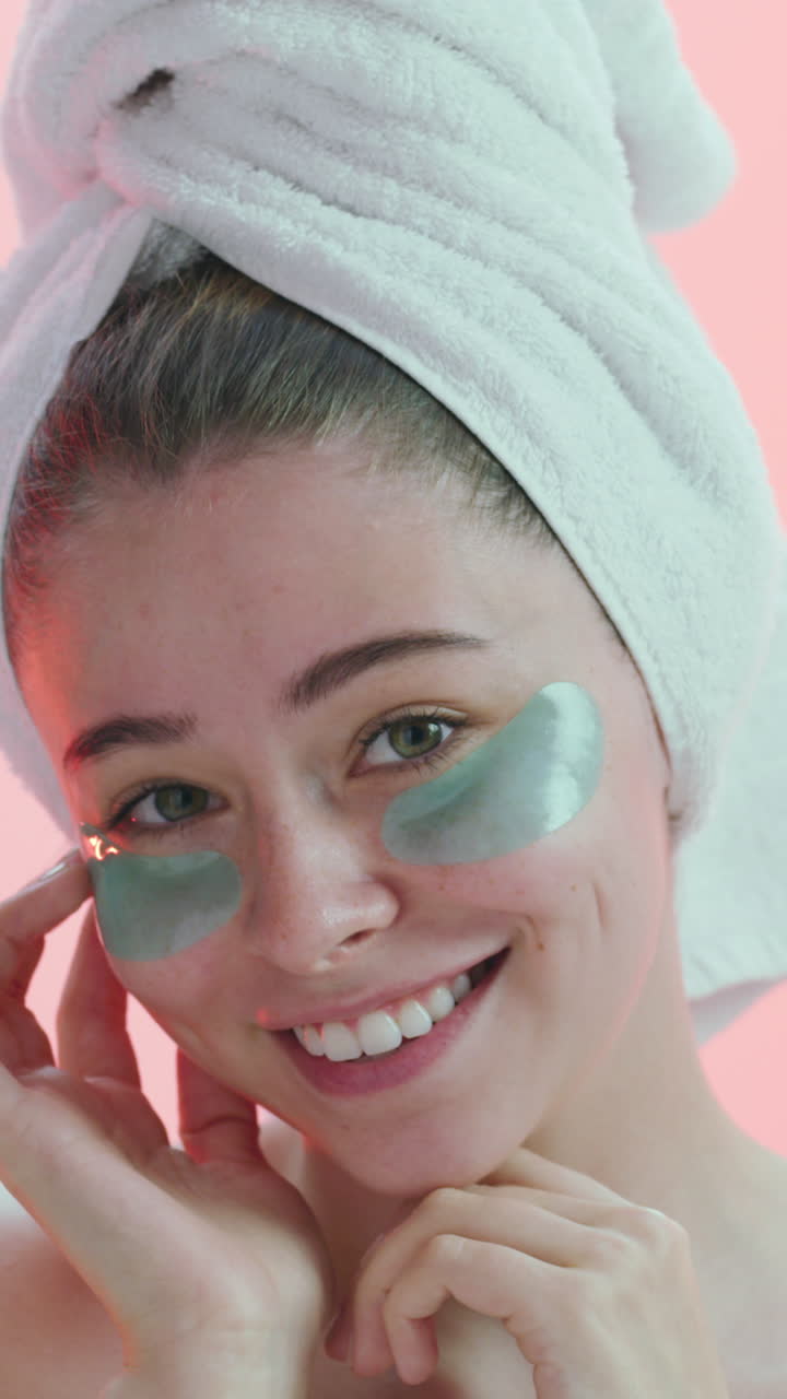 Jonge vrouw met oogmaskers en handdoek die lacht voor huidverzorging