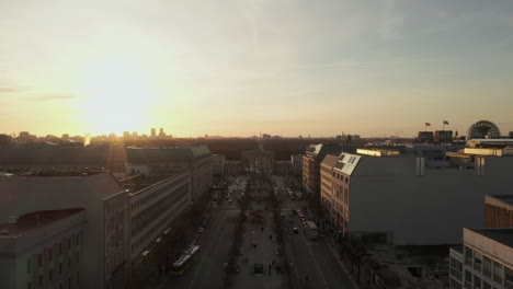 AERIAL:-Scenic-low-flight-through-busy-Berlin,-Germany-Street-towards-Brandenburg-Gate-in-beautiful-golden-sunset-light