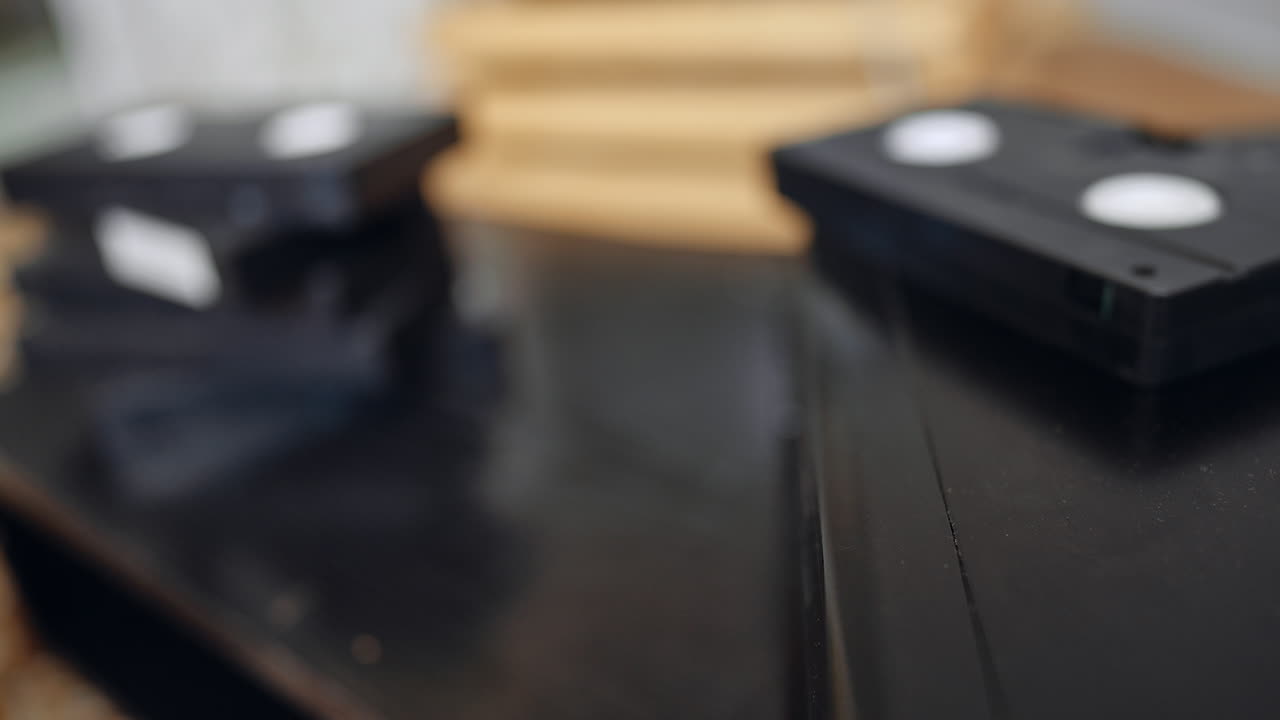 VHS-kasette på en videoafspillers overflade. En videokassette ligger delvist inde i en videoafspiller med et sløret fjernsyn bagved