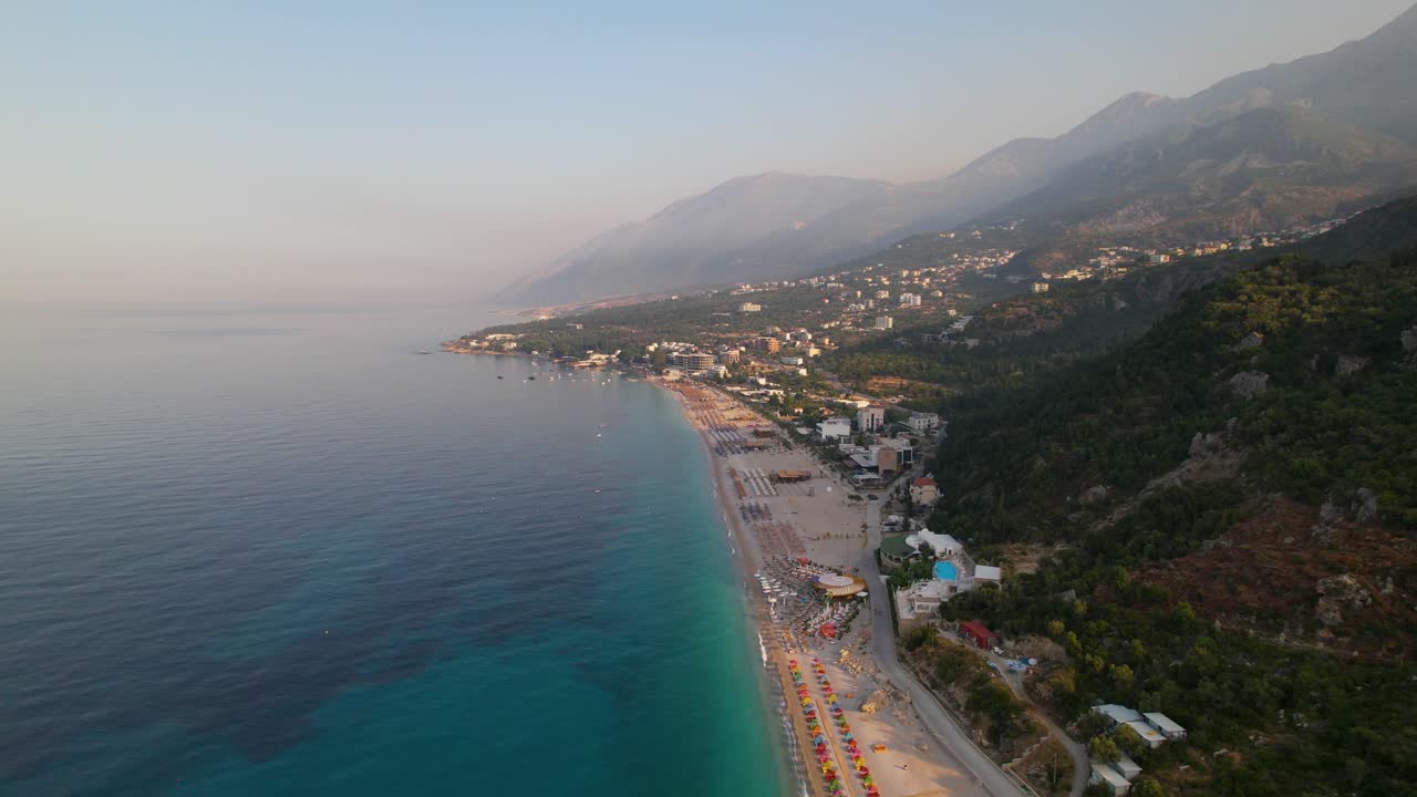 Beach of Dhermi with umbrellas and resorts on shore washed by blue turquoise sea water