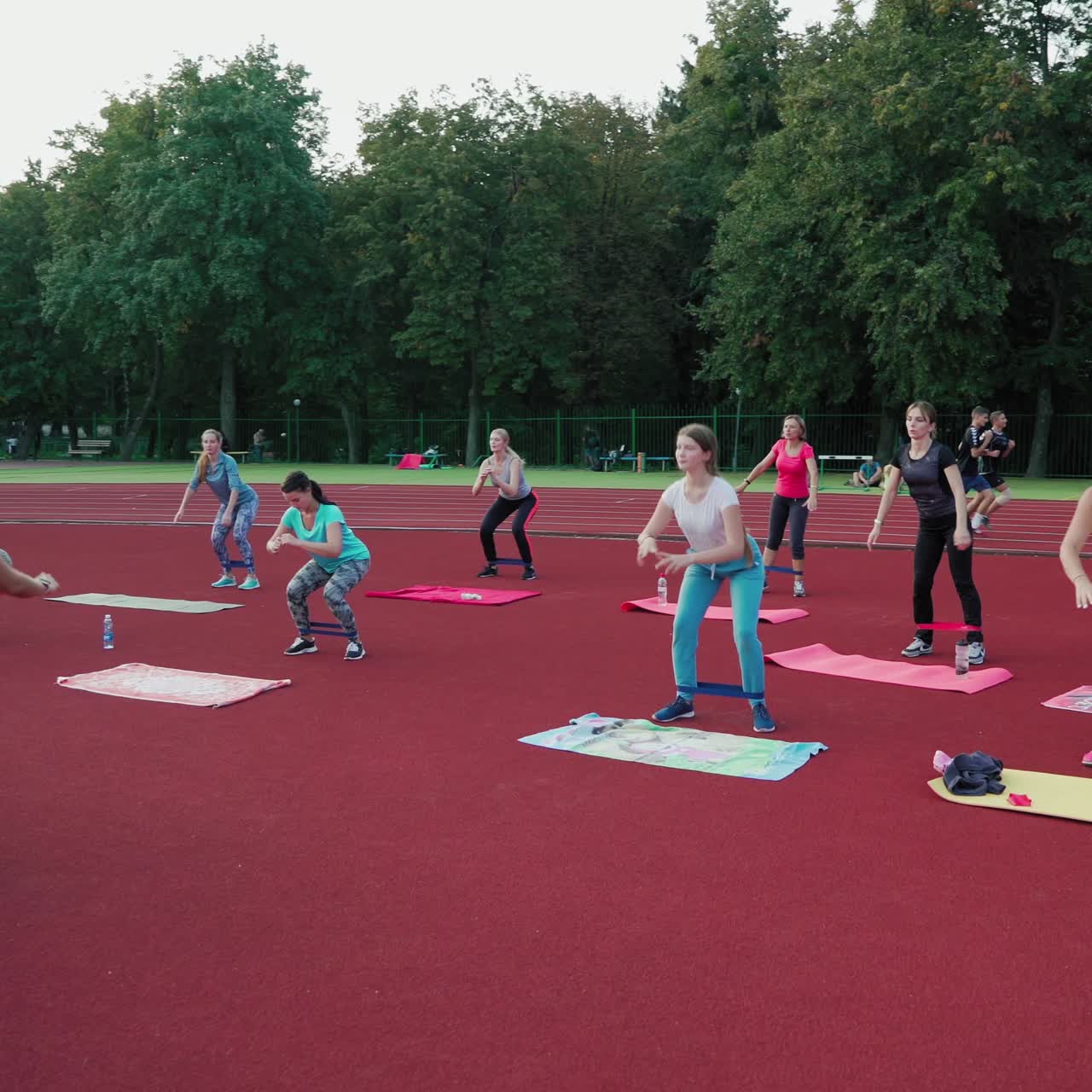Female team training on the outdoor stadium. Group of women doing exercises with fitness rubber on the modern sports ground. Healthy lifestyle.