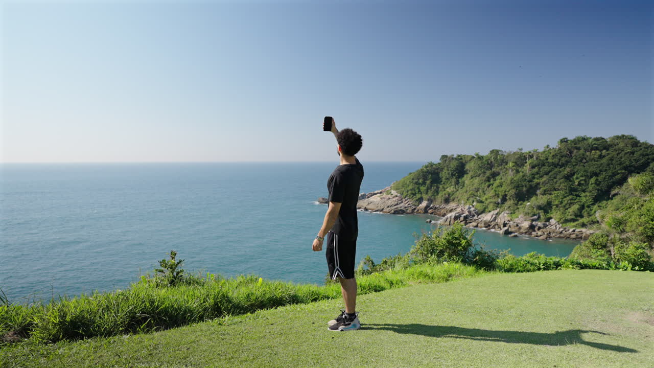 Lonely man standing on edge of cliff looking for signal with smartphone