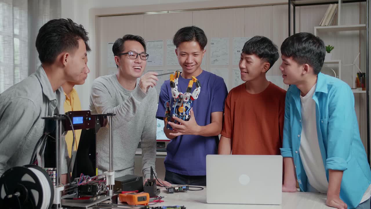 노트북과 3d 프린팅을 가진 아시아 남자가 학교에서 소년들에게 사이보그 손을 사용하는 방법을 설명합니다.