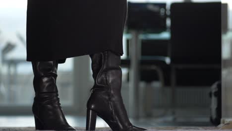 a-businesswoman-in-a-dress-wearing-shiny-black-boots-walks-towards-the-camera-and-then-presents-her-boots,-zoom-out