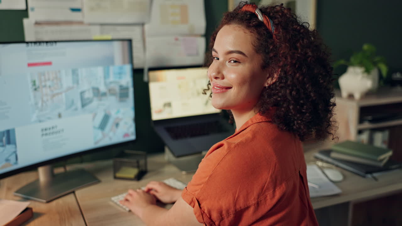 A woman smiles as she works on her computer at her desk