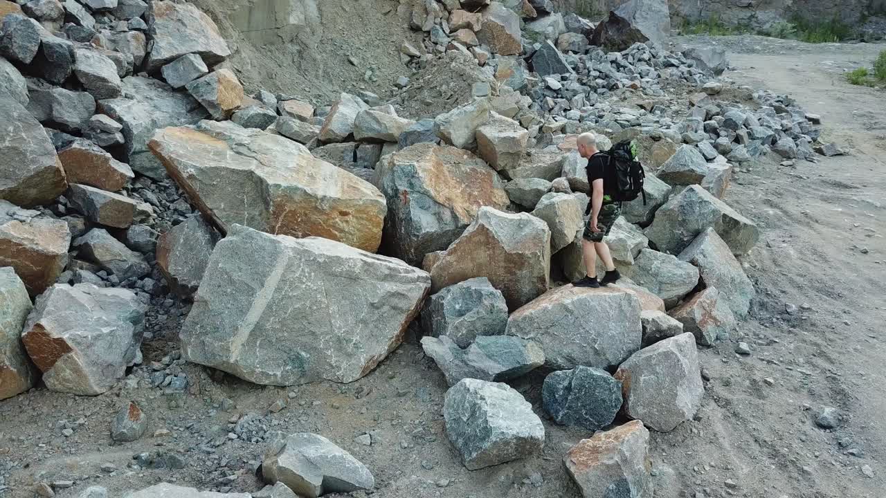 Active tourist climbing on a big pile of stones in the mountainous area. Scenic view of rocky cliff and a young man hiker walking on that place. Camera moves up.