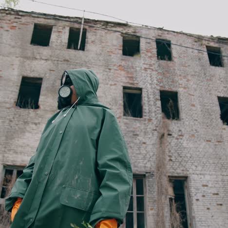 environmentalist in protective suit and gas mask. man in gas mask near abandoned destroyed building