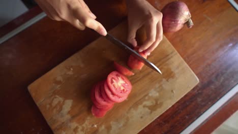 cutting tomato slices on wooden cutting board, female hand, top view