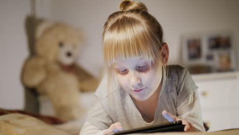 Portrait-Of-A-Child-Enjoying-A-Tablet-With-A-Bedroom-Lies-On-His-Bed-In-The-Evening