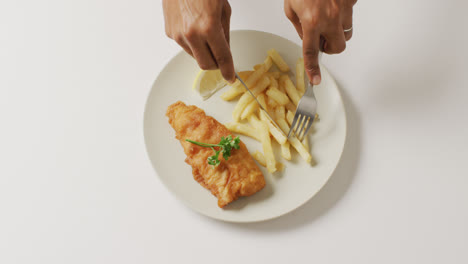 video overhead shot of african american hands eating fish and chips on white plate with copy space