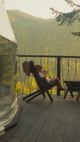 siblings watch movies on modern smartphones overlooking forest and mountains. adorable kids enjoy spectacular view on terrace surrounded by untouched nature