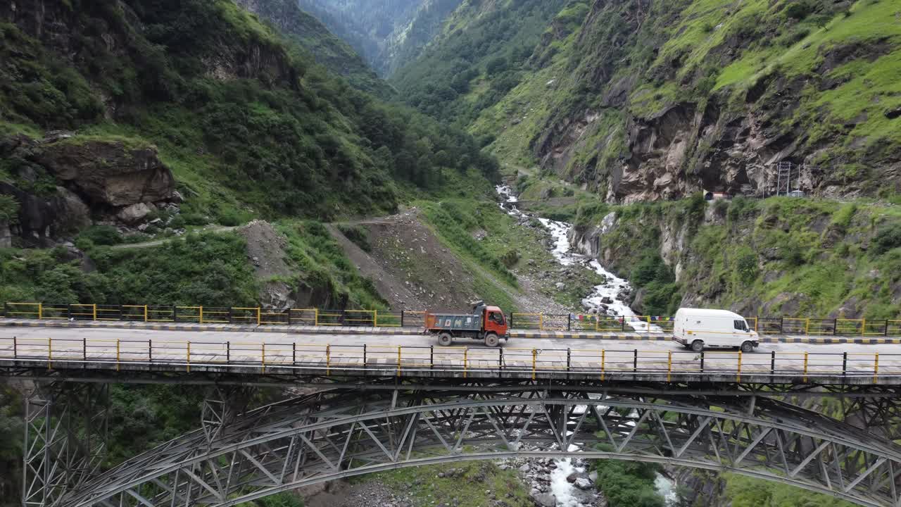 un dron de vehículos comerciales que viajan en un puente suspendido en un valle fluvial en la remota carretera de himachal pradesh, en las estribaciones del himalaya indio