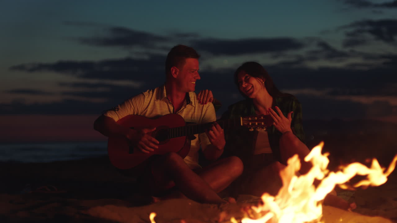 해가 지는 해변에서 캠프불 에서 기타를 연주하는 부부