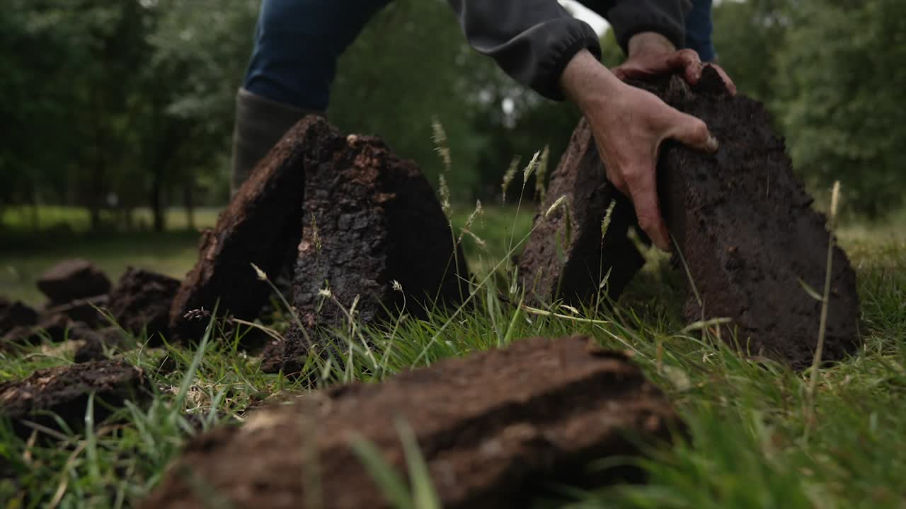 En person stabler traditionelle tørvebrikker på en mark for at lufttørre, en traditionel metode til at høste brændsel i Irland og Skotland.
