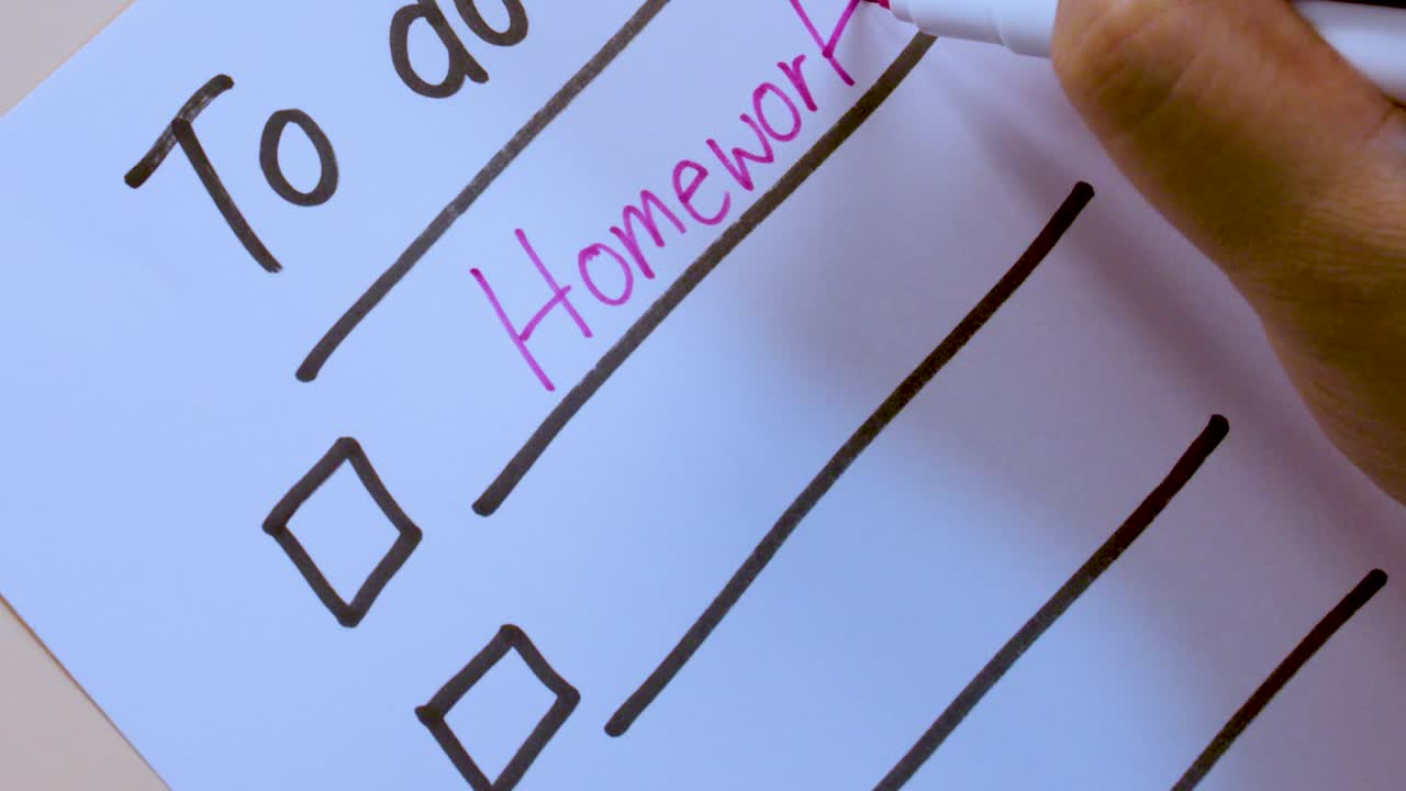 Una persona usa un pennarello rosa per scrivere i compiti su una lista di controllo di carta, in primo piano.
