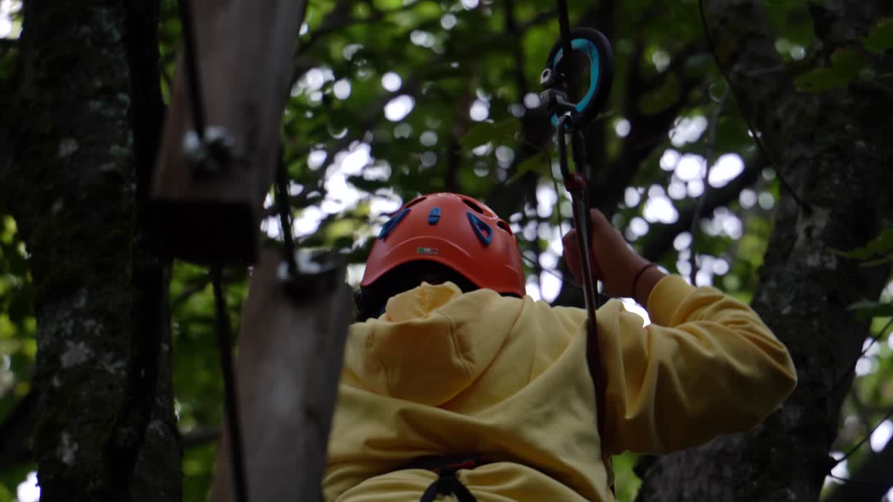 niño valiente atraviesa las cuerdas colgando del árbol con el equipo de seguridad en un entrenamiento de escalada
