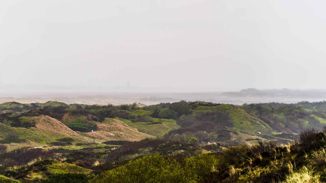 Timelapse of fog and rain swiping over expansive grassy covered sand dunes on the German island of Spiekeroog (East Frisian Islands) located in the North Sea.